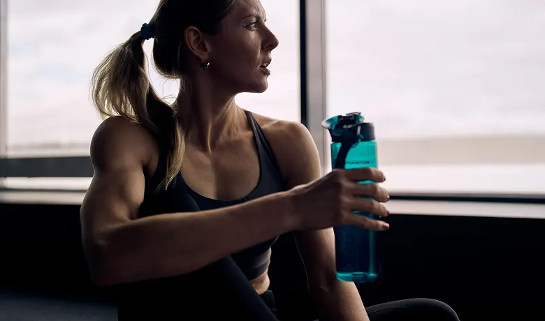A women in workout clothes staring out a window with a water bottle in hand.