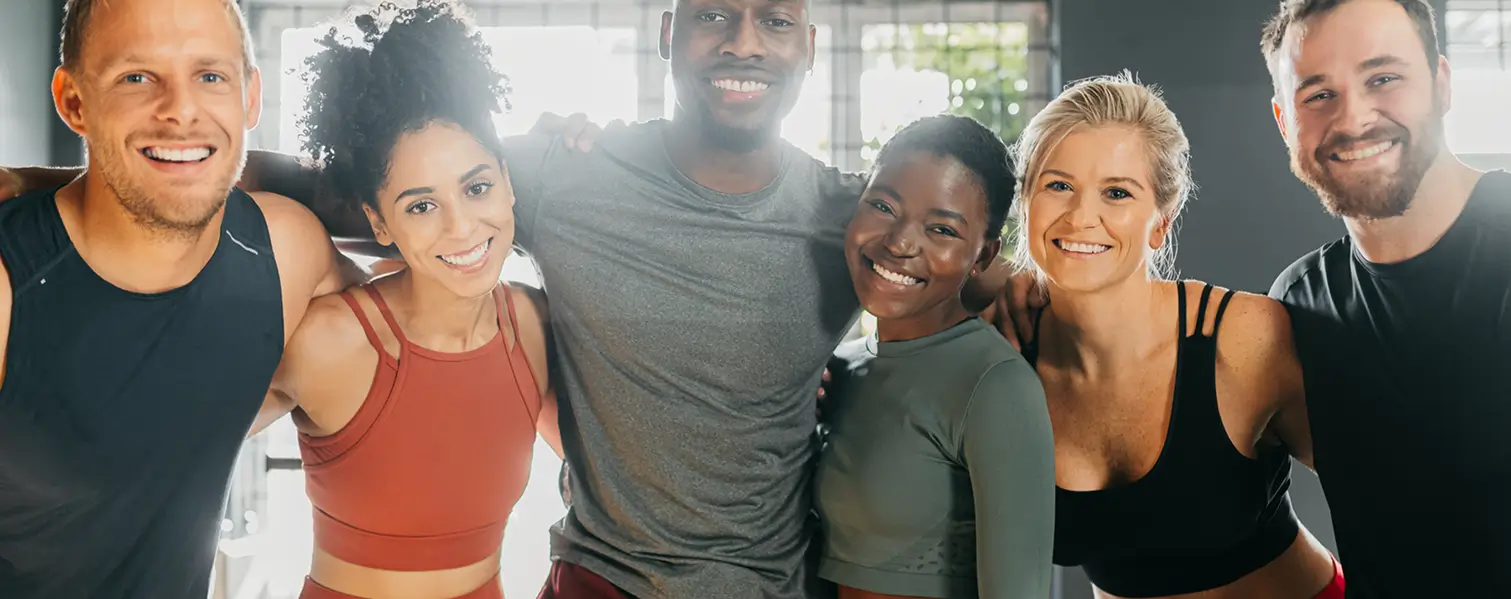 A group of smiling men and women in exercise clothes in a gym, taking a self-portrait photograph.
